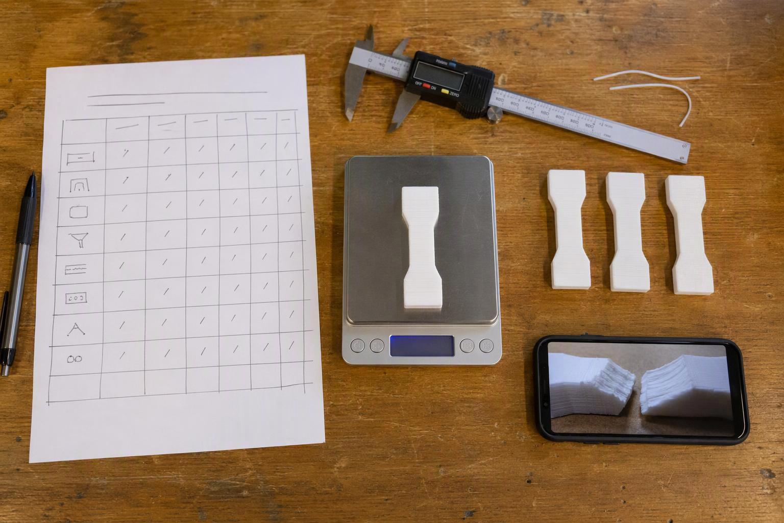 Makerspace test bench with a printed test log, caliper, scale and printed coupons ready for comparison