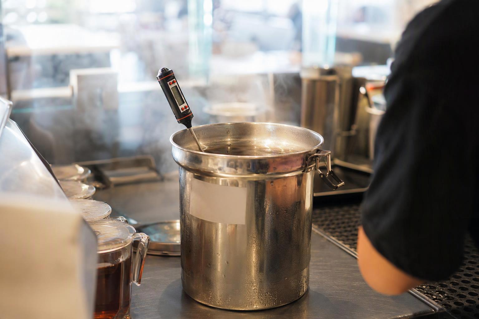 a holding vessel on a counter with a marked discard-time label and a probe thermometer reading above 135°F